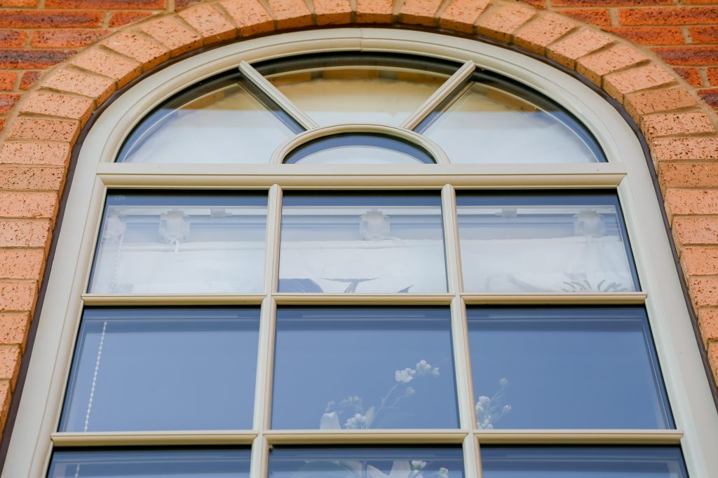 Cream arched PVCu window with Georgian glazing bars installed in a traditional brick home