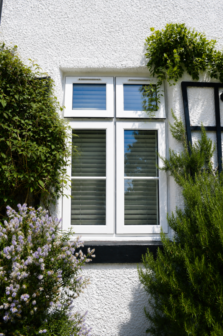 White uPVC casement windows on a white textured house exterior with garden plants and modern energy-efficient glazing.