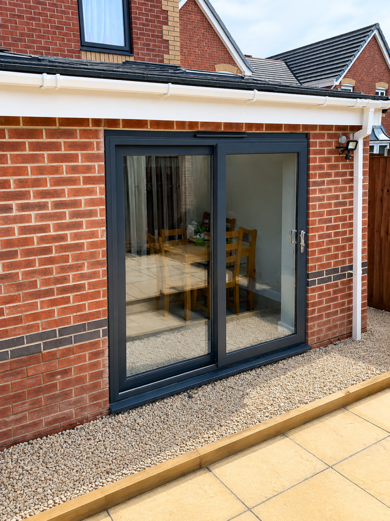 Anthracite grey uPVC sliding patio doors installed on a modern brick home, providing secure, energy-efficient access to the garden with large glazed panels for maximum natural light.