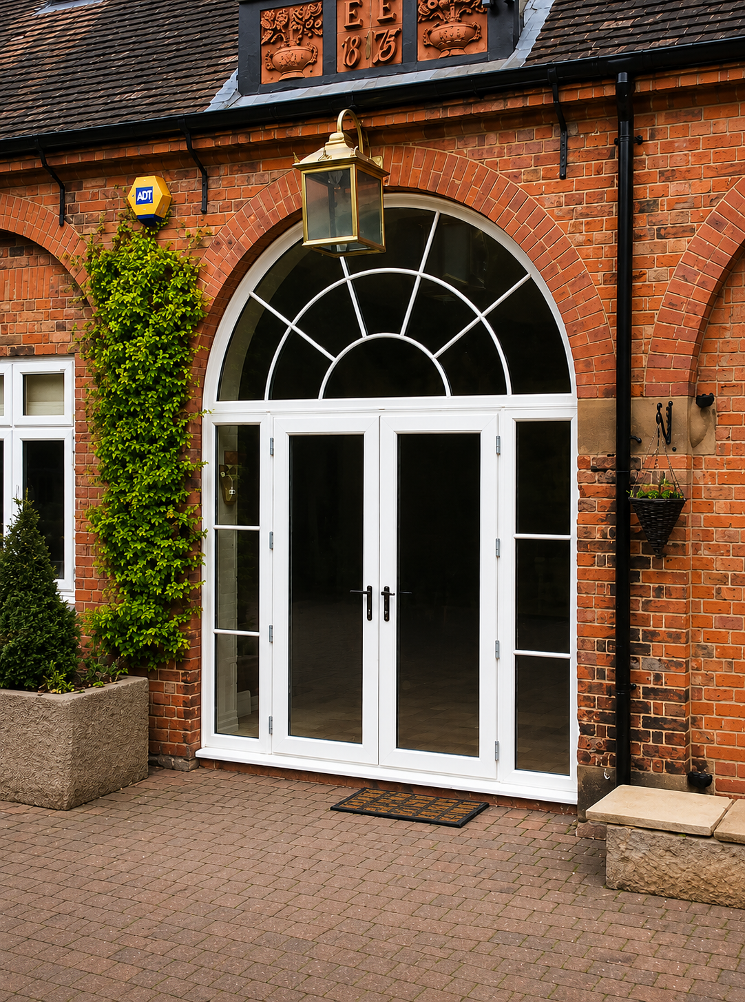 White uPVC French doors with matching sidelights and an arched fanlight, installed within a traditional red brick home entrance.