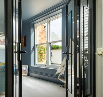 Sliding sash window in a stylish blue-painted interior with views of a brick house and garden.