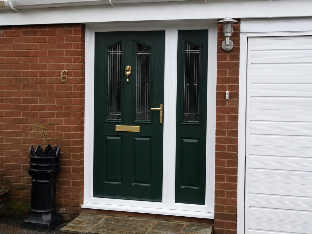 Dark green composite front door with decorative glazed panels and matching sidelight, finished with gold hardware and a white frame on a traditional red brick home.
