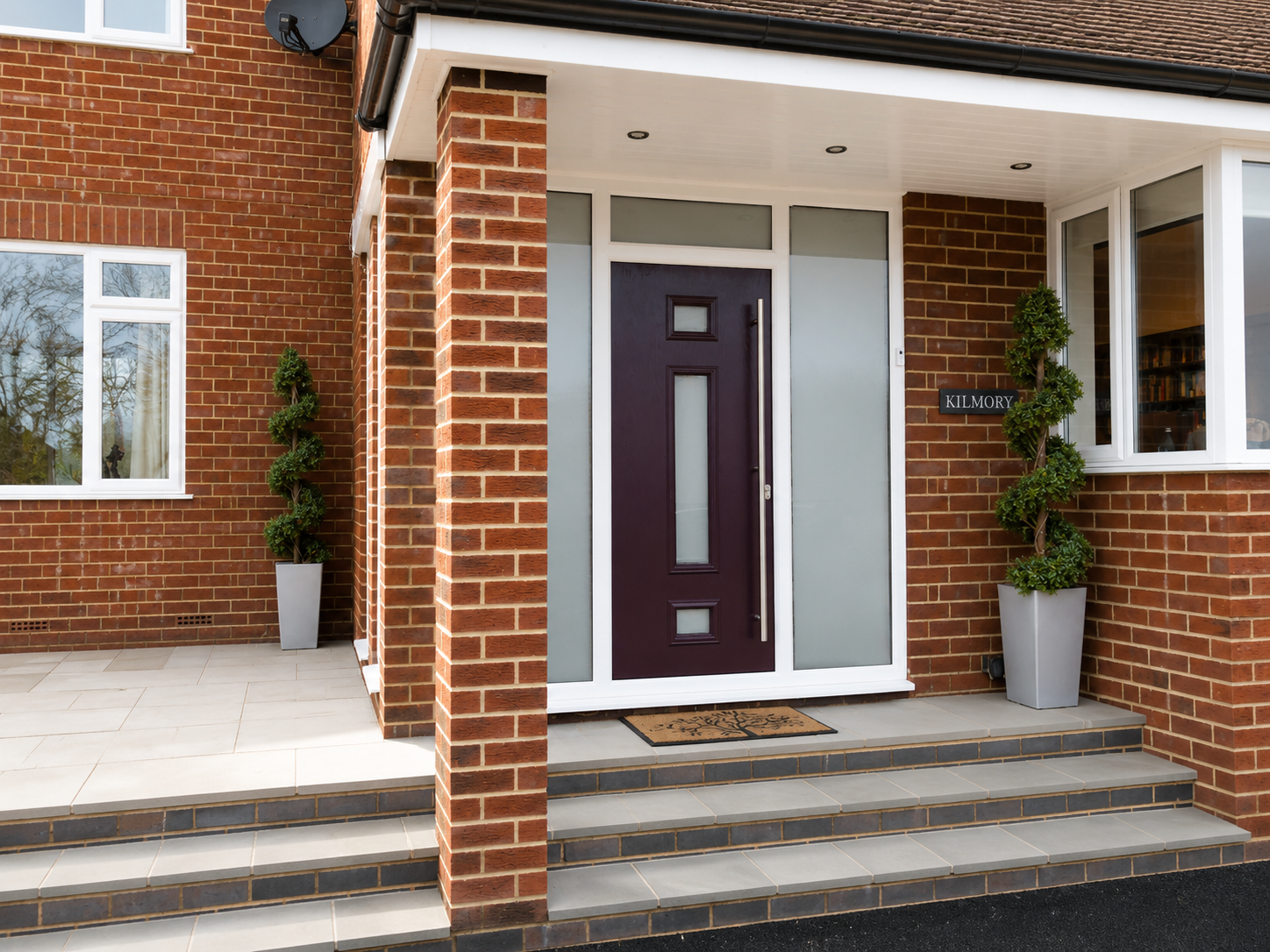 Plum composite front door with frosted glazed panels and matching side lights, finished with a long stainless steel pull handle, set within a modern brick porch entrance.