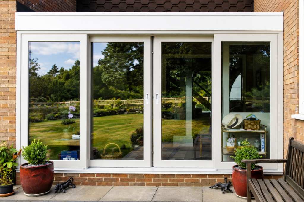 White aluminium sliding patio doors with fixed side panels, opening onto a paved patio and landscaped garden, bringing natural light into the home.