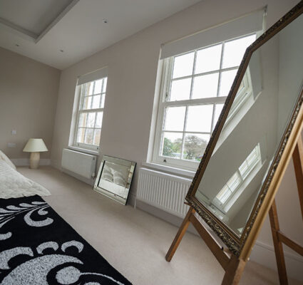 White sliding sash windows in a bright bedroom with a large ornate floor mirror.
