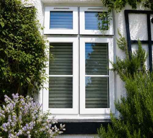 White uPVC casement windows on a white textured house exterior with garden plants and modern energy-efficient glazing.
